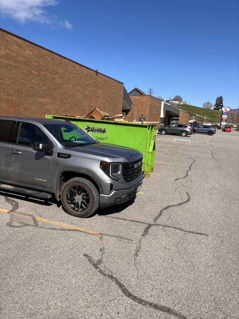 Grey pickup beside a green roll-off bin in a parking lot, illustrating fleet renewal and end-of-life recycling.