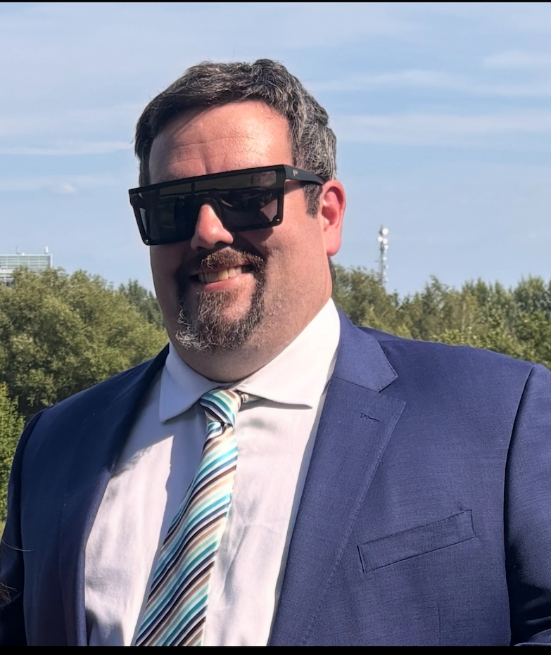 Portrait of TNT’s demolition specialist COO in a blue suit and striped tie, wearing sunglasses outdoors.