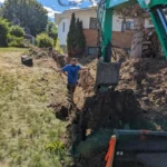 Excavator trenching and backfilling on a residential slope in Kelowna, BC