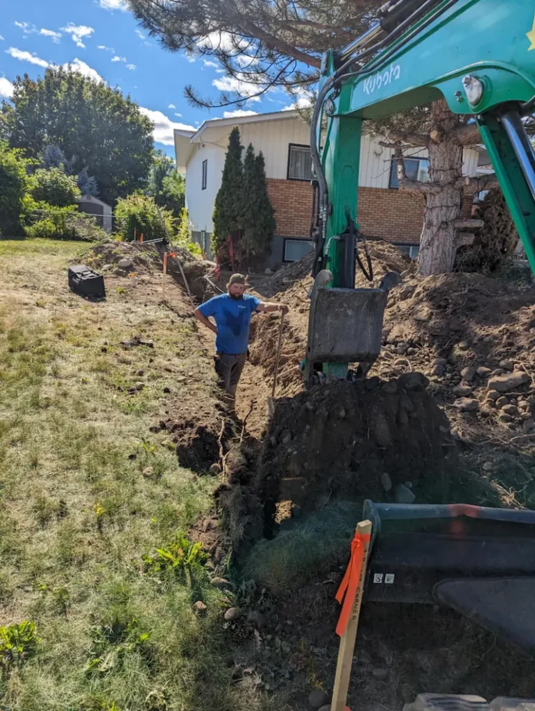 Excavator trenching and backfilling on a residential slope in Kelowna, BC