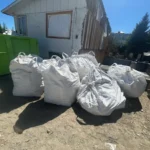Bulk bags of construction debris beside a green dumpster at a residential renovation in Kelowna, ready for TNT junk removal pickup.