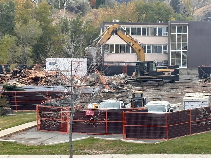 Excavator dismantling a commercial building behind safety fencing in Kelowna, BC