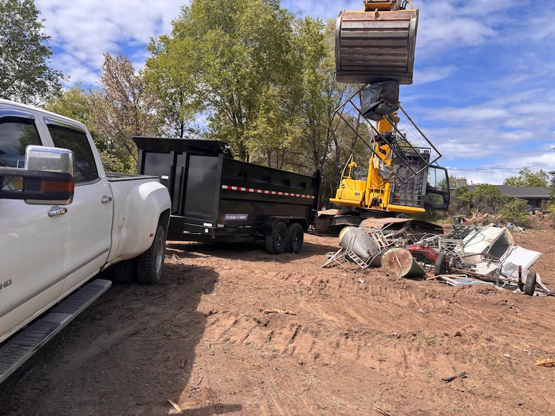 Excavator loading scrap metal into a dump trailer during debris removal and recycling in Kelowna, BC