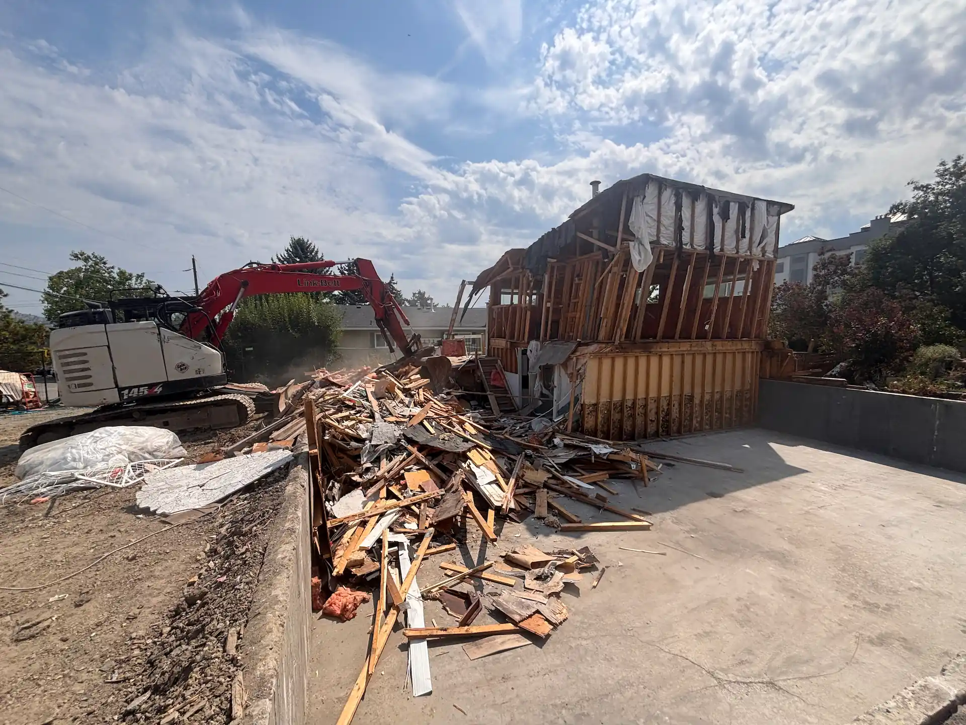 Excavator tearing down a house with debris piled on site in Kelowna, BC.