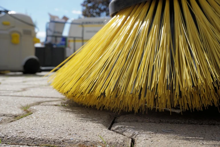 Close-up of a yellow industrial street sweeper brush cleaning paved stones outdoors.